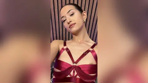 LuanaRodgers poses in a red strappy lingerie set with her dark hair pulled back in a sleek style.
