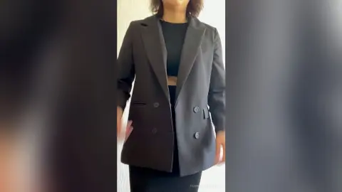 PenneySteinfeldt wears a black blazer over a black crop top while standing against a white wall.
