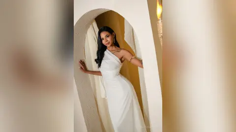 Elegant woman in a white satin gown posing gracefully in a minimalist arched doorway with warm lighting.