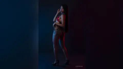 Young woman in red bikini top and brown shorts posing in moody, cinematic studio lighting.