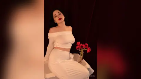 Elegant woman in a white off-the-shoulder dress posing with red roses against a moody dark background.