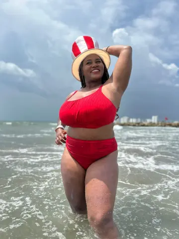 Smiling woman in a red bikini and straw hat enjoying a sunny day at the beach in the ocean waves.