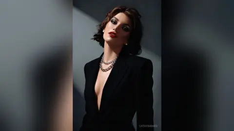 Elegant woman in a black blazer and silver chain necklace posing with bold red lips in dramatic studio lighting.