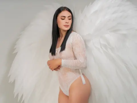 Elegant woman in white lace bodysuit wearing large white angel wings in a dreamy studio setting.