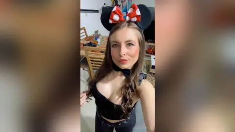 Smiling woman wearing Minnie Mouse ears and a black outfit in a cozy home setting.