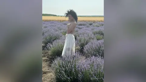 Dreamy woman in a white lace dress standing in a blooming purple lavender field under a clear sky.