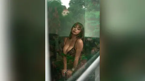 Glamorous woman in a black lace bralette posing in a lush, moody garden setting.