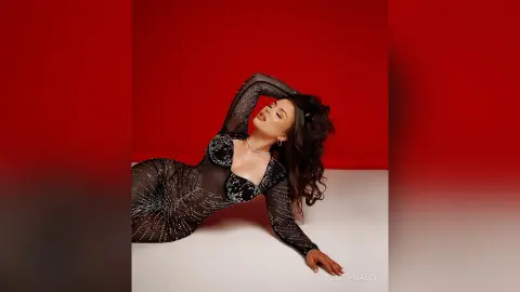 Elegant woman in a sparkling black sheer gown posing against a bold red background.