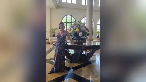 Elegant woman in a floral maxi dress standing by a large flower arrangement in a luxury hotel lobby.