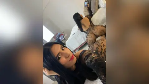 AnnMyer shows off her curves in a black lace bodysuit while posing on a bed with her long black hair down.