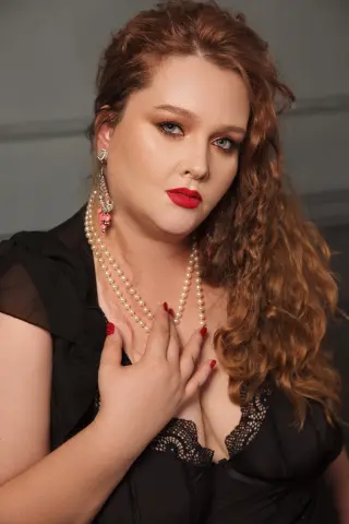 Redheaded woman in a black lace dress and pearl necklace posing with a glamorous, elegant mood.