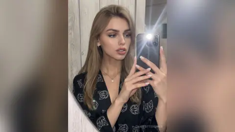 CharlotteReimer takes a mirror selfie wearing a black patterned top with her long blonde hair down.