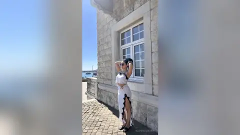 Stylish woman in a white cutout maxi skirt and crop top posing by a stone building on a sunny day.