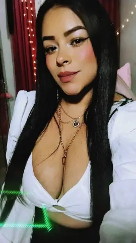 DanielaJames poses in a white low-cut top, showing cleavage, with her long black hair falling over her shoulders.