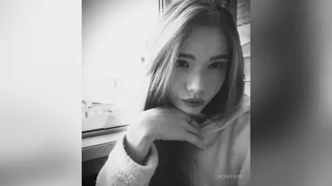 Young woman in a cozy white sweatshirt posing with a thoughtful expression in a bright indoor setting.