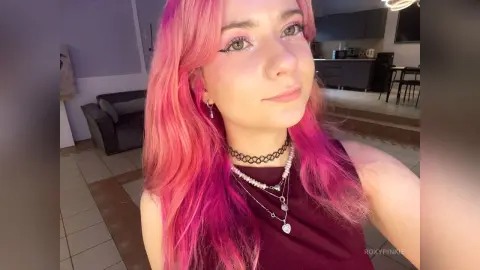 Young woman with pink hair and black choker smiling in a modern living room setting.