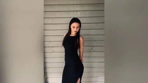 Elegant woman in a sleek black midi dress posing against a grey wood paneled wall with a moody aesthetic.