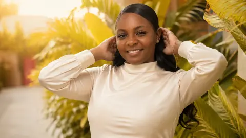 LilyReeds smiles while posing outdoors in a cream long-sleeve top with her hands behind her head.