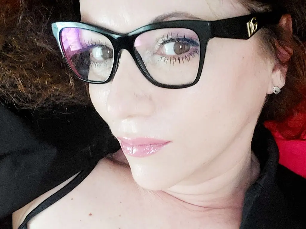 Close-up portrait of a woman with glasses and diamond earrings looking calm in a dark setting.