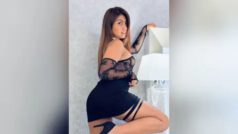 Elegant woman in a black lace mini dress posing confidently in a bright, modern indoor setting.