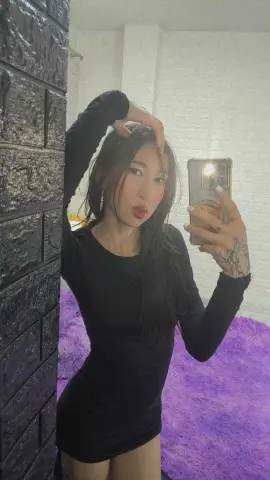 Young woman in a black long-sleeve dress taking a moody mirror selfie in a modern room.