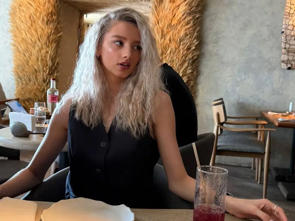 Blonde woman in a black sleeveless top sitting at a cafe table with a relaxed, thoughtful mood.