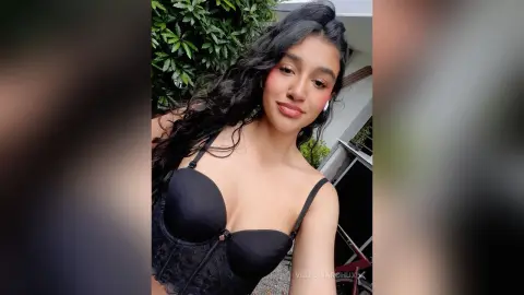 Young woman with long wavy hair wearing a black lace corset top outdoors in a natural setting.