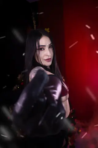 Mysterious woman in dark gothic attire with long black hair posing in a moody red and black setting.
