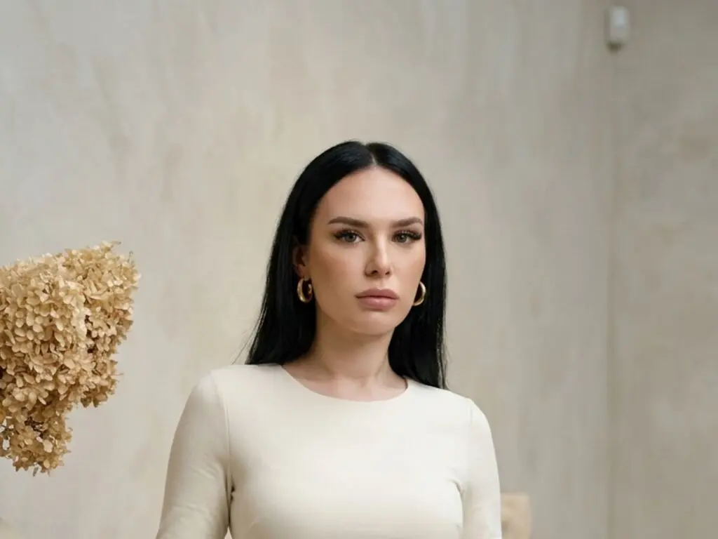 AmeliaCallens poses in a white long-sleeve top with her long black hair down and gold hoop earrings.