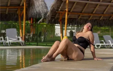 Relaxed woman in black bikini lounging by a tropical resort swimming pool on a sunny day.