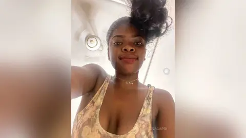 Young Black woman in a floral halter top taking a selfie in a bright, modern bathroom.