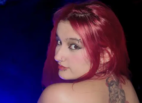 Young woman with vibrant pink hair and nose piercing posing in moody blue lighting.