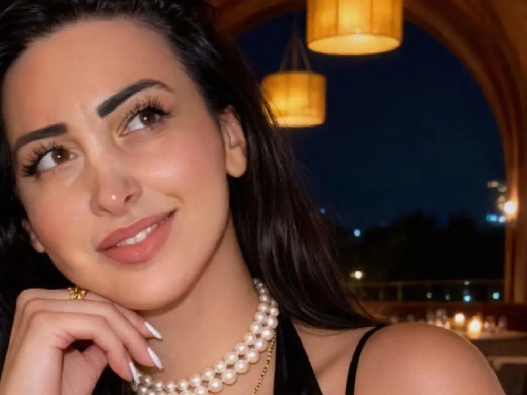 Smiling woman in a black dress and pearl necklace enjoying a romantic evening at an outdoor terrace restaurant.