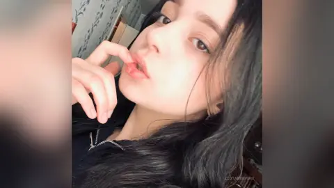 Close-up portrait of a young woman with long dark hair wearing a black top in a soft, natural indoor setting.