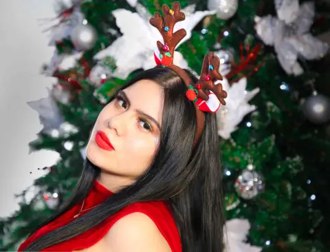 Young woman with reindeer antlers posing in front of a festive Christmas tree with a holiday mood.