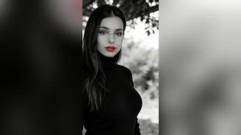 Elegant woman in a black turtleneck sweater posing with red lips in a soft outdoor setting.