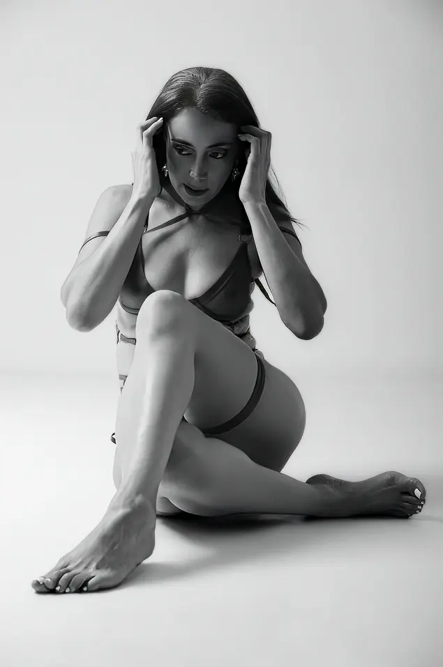 PrettyLady74 — Elegant woman in minimalist lingerie sitting on a white floor in a moody black and white studio portrait.