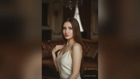 Elegant woman in a white silk slip dress posing in a moody, vintage luxury interior.