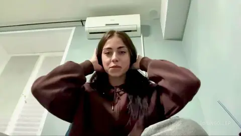 Young woman in a brown hoodie wearing headphones in a bright room with a relaxed mood.