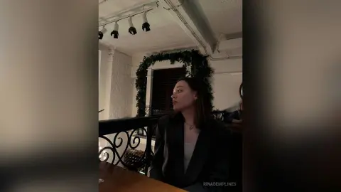 Elegant woman in a black blazer sitting in a moody, rustic cafe with greenery decor.