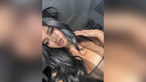 NicoleBella poses with her long black hair falling over her shoulder, wearing a black bra and a gold choker necklace.