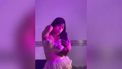 Young woman in a white lace corset top posing in moody purple lighting for a stylish selfie.