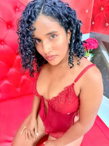 Young woman with curly hair in a red lace camisole sitting on a red tufted sofa in a romantic mood.