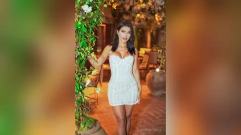 Elegant woman in a white lace mini dress posing in a warm, romantic garden setting at night.