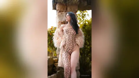 Elegant woman in a leopard print bodysuit and faux fur coat posing by stone ruins in soft natural light.