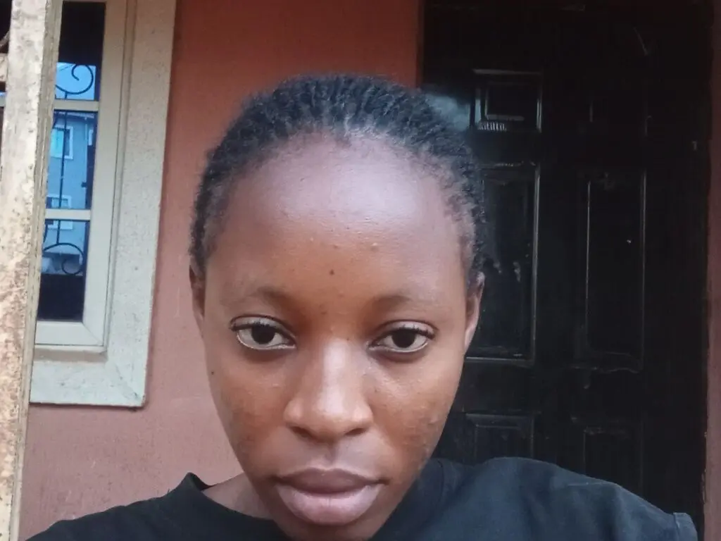 Close-up portrait of a young woman with braided hair wearing a black shirt in a natural outdoor setting.