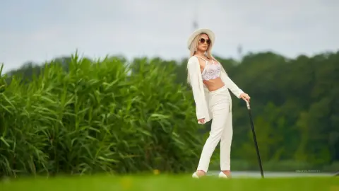 Anastasia stands outdoors in a white lace bra and matching white trousers, wearing a white hat and sunglasses.