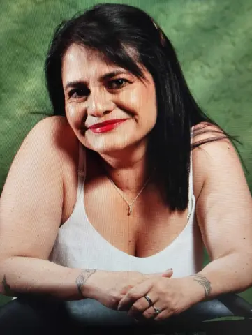 Smiling woman in a white tank top posing against a green background for a cheerful portrait.
