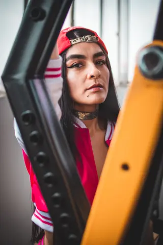 Young woman with long dark hair wearing a red cap and choker posing in a bright indoor setting.