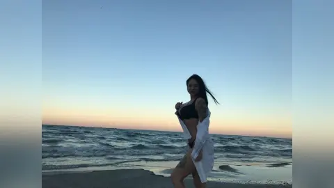 DeeaAnderson stands on a beach at sunset wearing a black bikini top and an open white shirt.